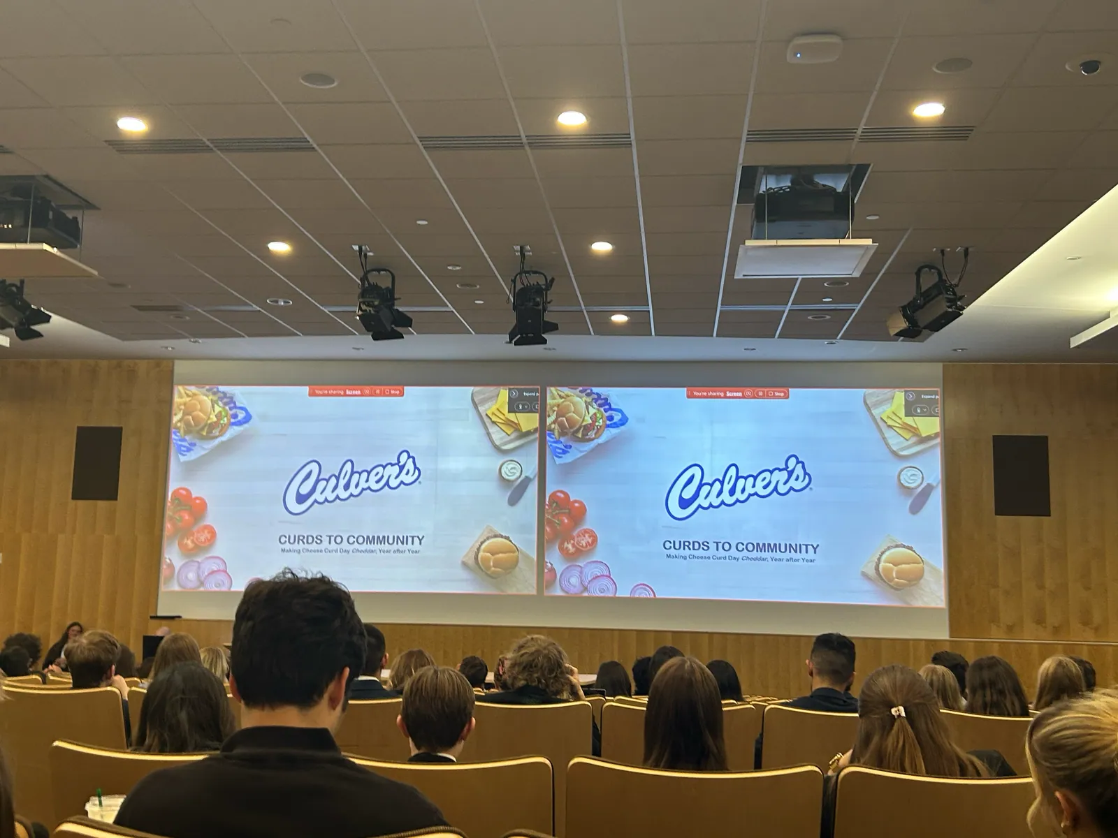Culver's Curds to Community title slides on two screens at the front of the auditorium.